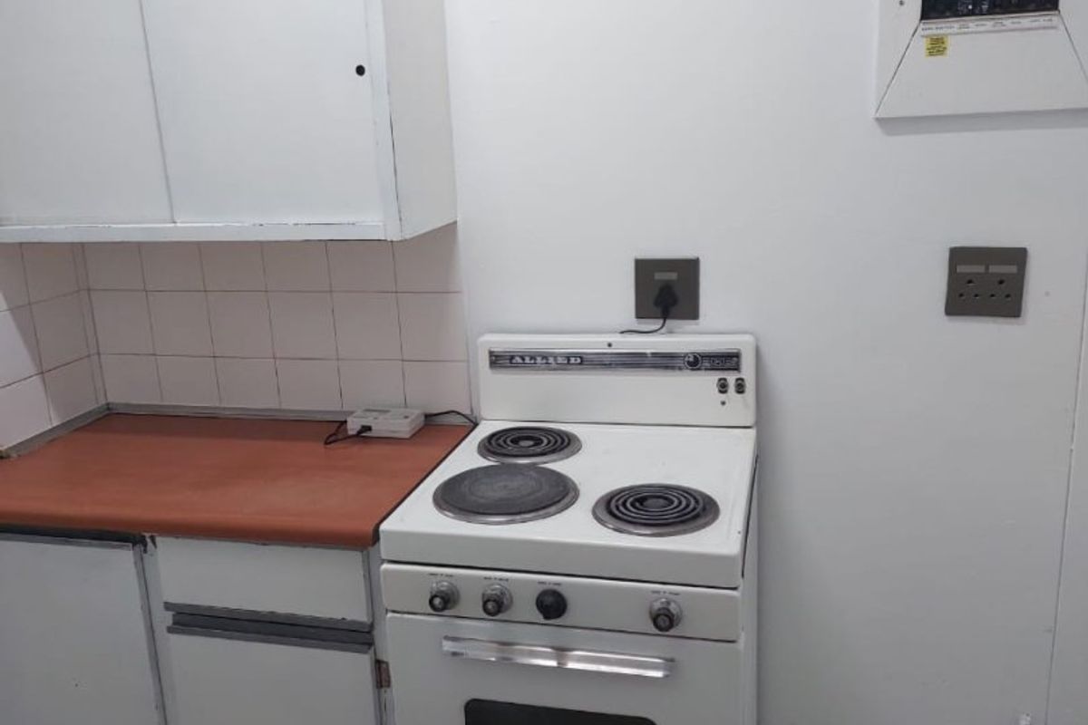 A compact kitchen area featuring basic cabinetry, a tiled backsplash, and a vintage freestanding electric stove with an integrated electrical distribution board.