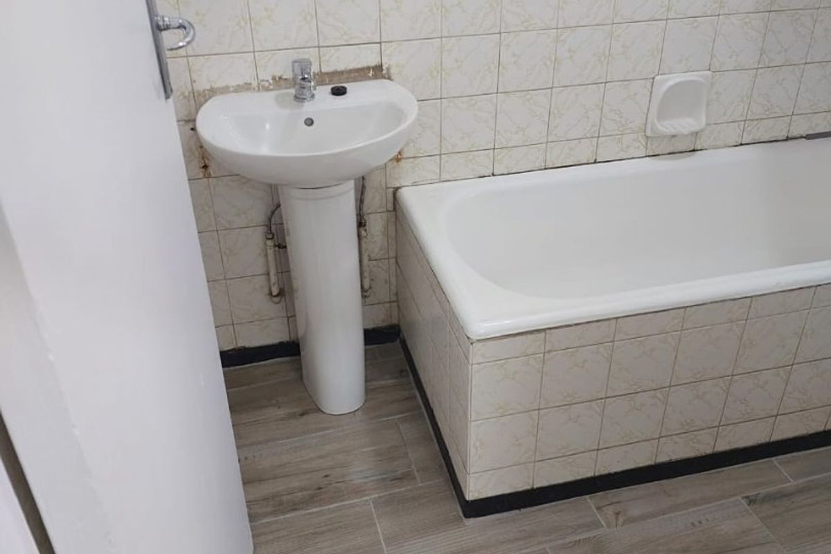 A functional bathroom featuring a pedestal basin, bathtub, and neutral tiled finishes. The space is ready for cosmetic updates to modernize the fixtures.