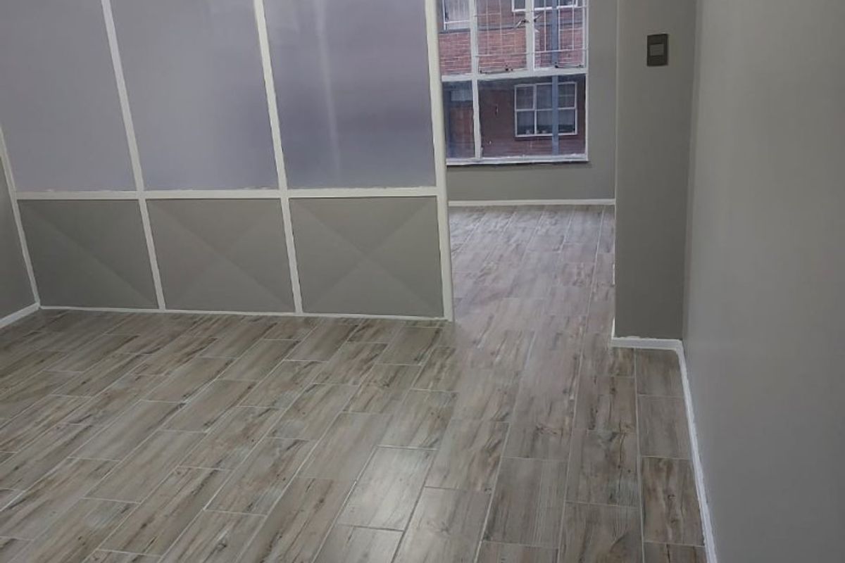 An empty living area featuring modern wood-look tile flooring and a semi-transparent partition wall, providing a clean and versatile space.