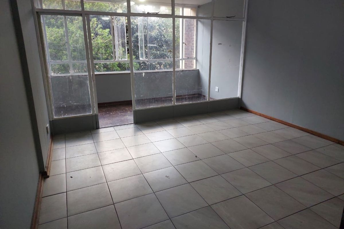 An empty living room featuring tiled flooring and a large glass partition leading to an enclosed balcony area.