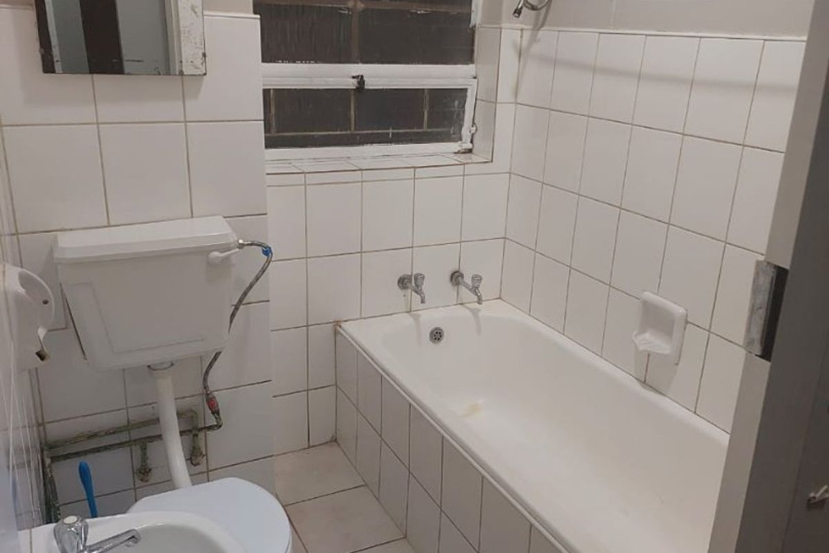 A compact bathroom featuring a standard bathtub, pedestal basin, and toilet with white wall and floor tiling, requiring cosmetic updates.
