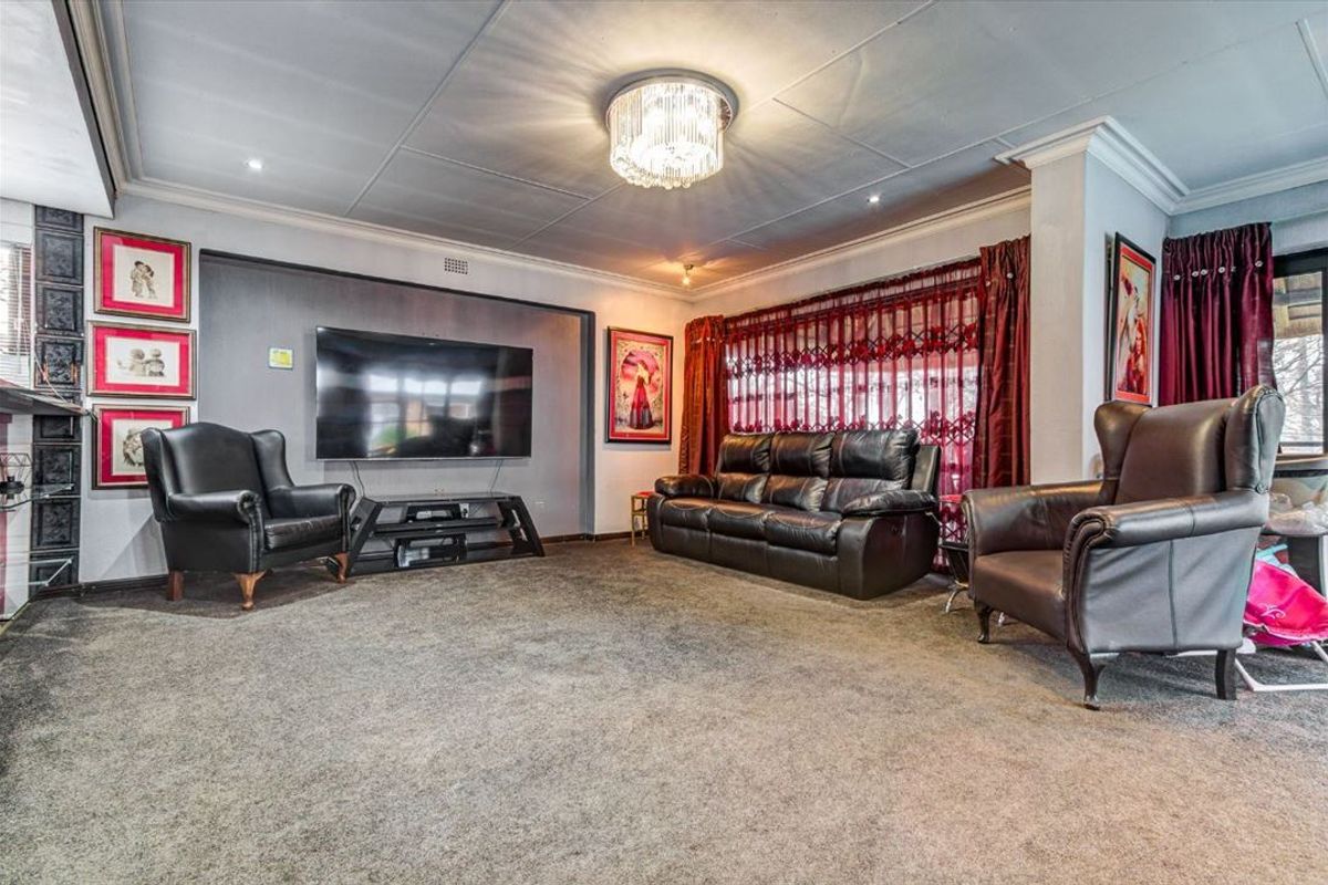 A spacious living room featuring a recessed media wall, coved ceilings with a decorative chandelier, and large windows fitted with security gates.