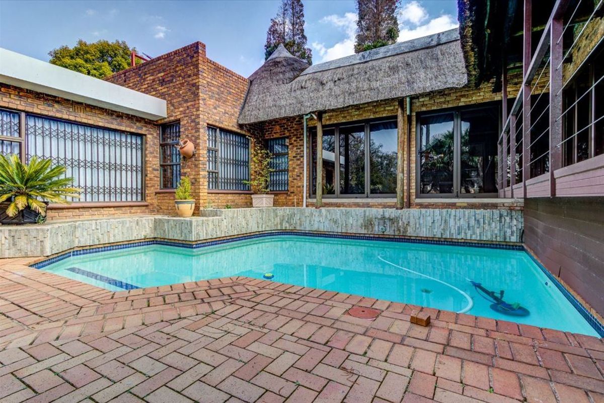 Outdoor pool area featuring brick paving, stone-clad pool surround, and a unique thatched roof structure with sliding door access to the home.