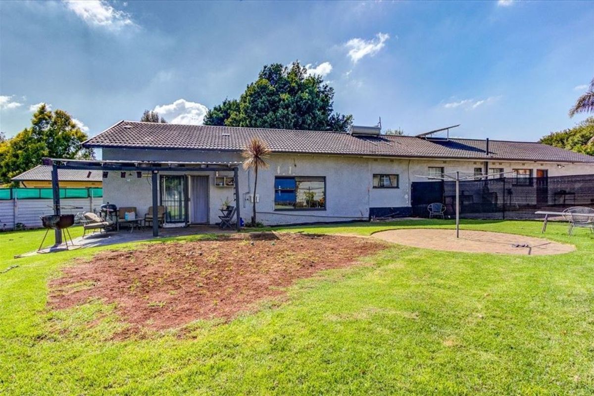 Rear view of the house featuring a tiled roof, solar geyser, covered pergola patio, and a spacious garden area.