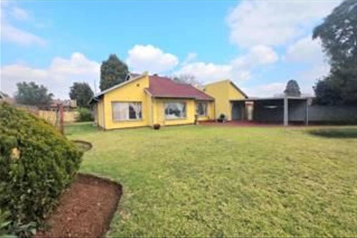 Rear view of the house featuring a yellow facade, tiled roof, and a covered patio area overlooking a spacious lawn and garden.