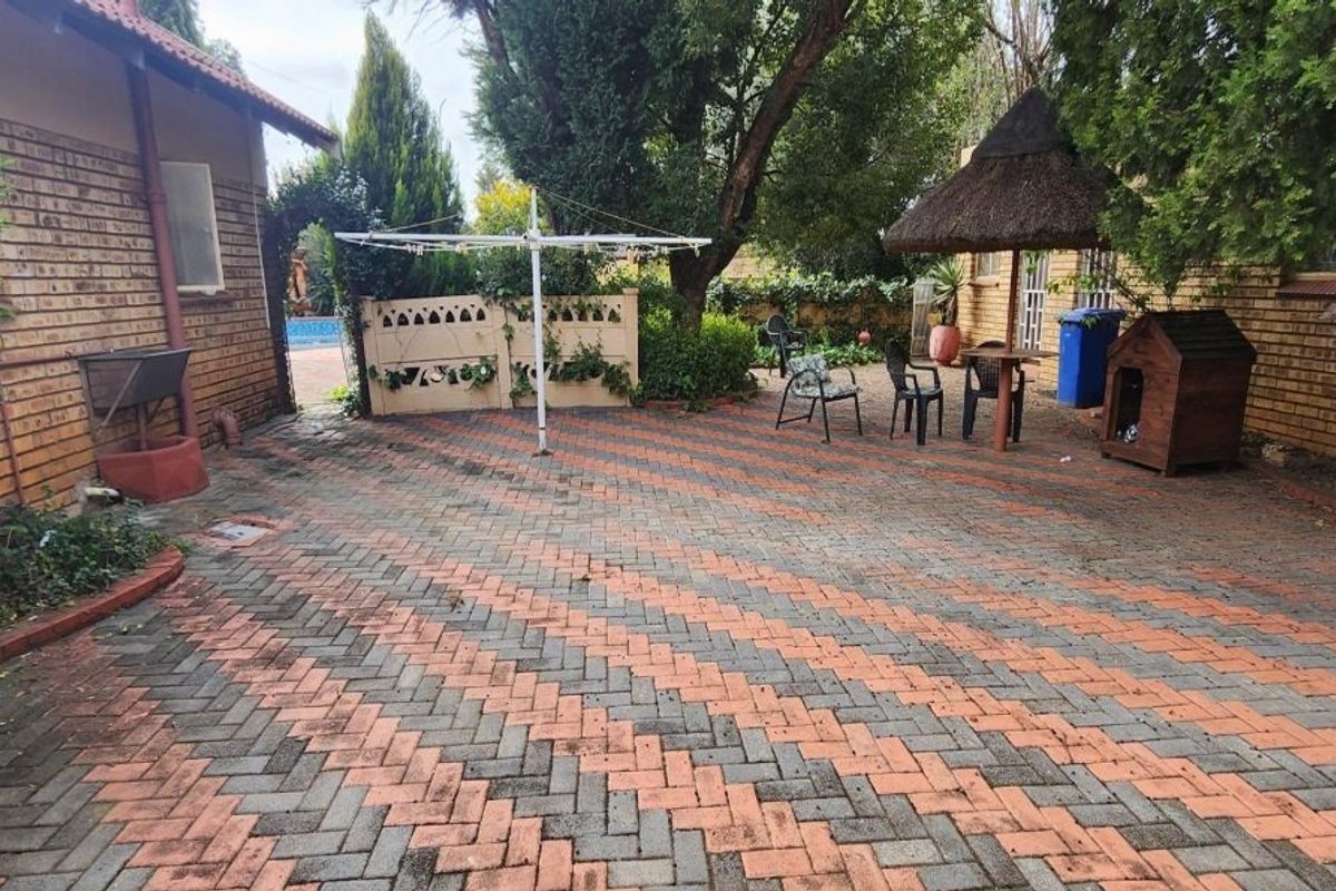 A rear courtyard area featuring herringbone brick paving, a small thatched lapa, and face brick exterior walls.