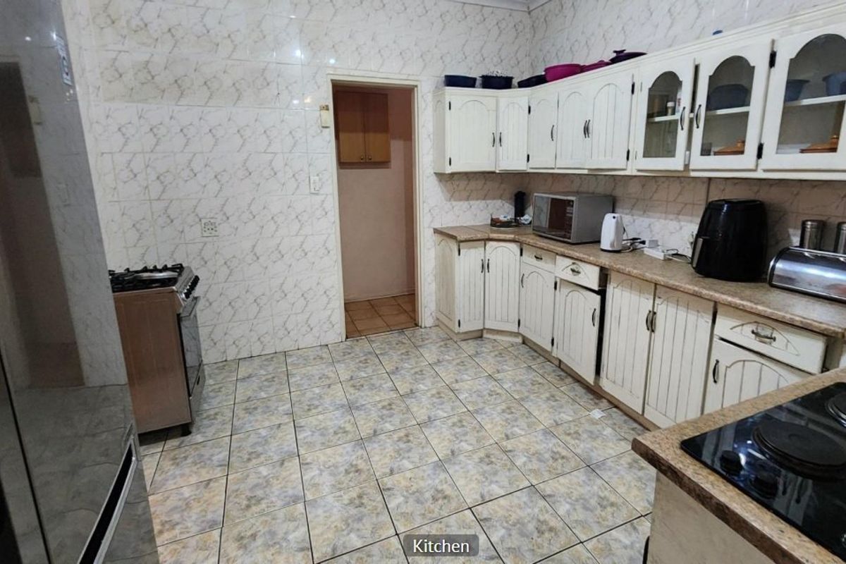 A functional kitchen featuring tiled walls and flooring, ample built-in cabinetry, and a combination of a freestanding stove and built-in hob.