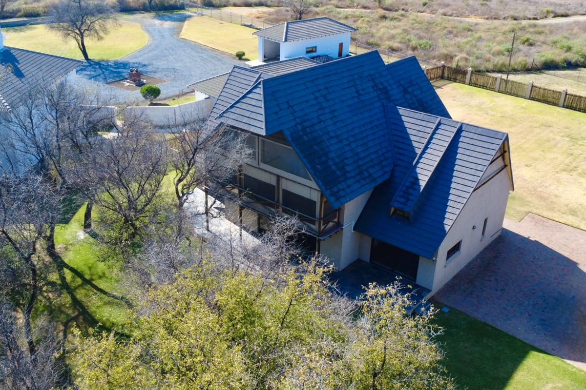 Aerial view of a multi-story farm property featuring a tiled roof, balcony, paved driveway, and a detached garage set on a spacious plot.