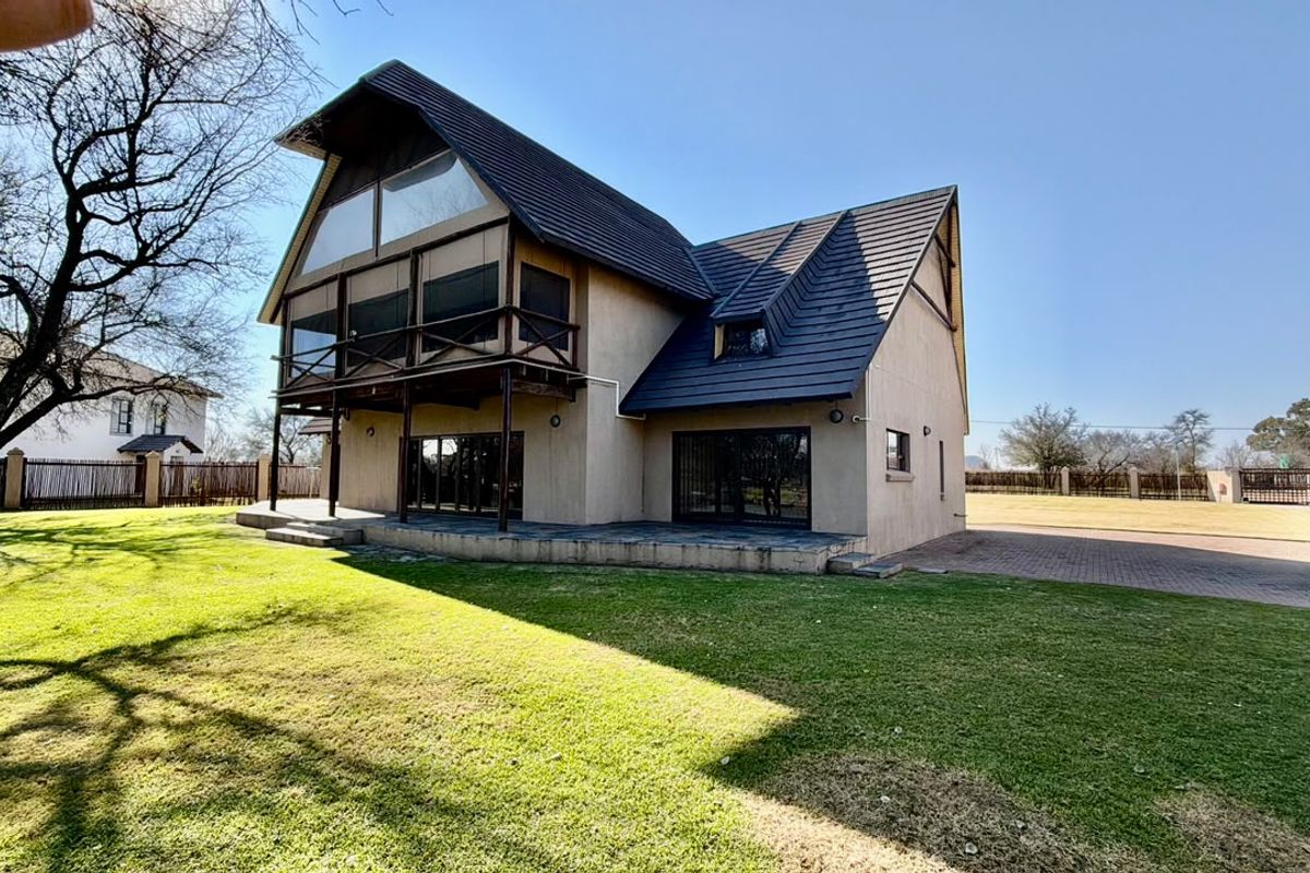 Rear view of a multi-story farm residence featuring a tiled roof, covered balcony with timber railings, and a paved patio area overlooking the garden.