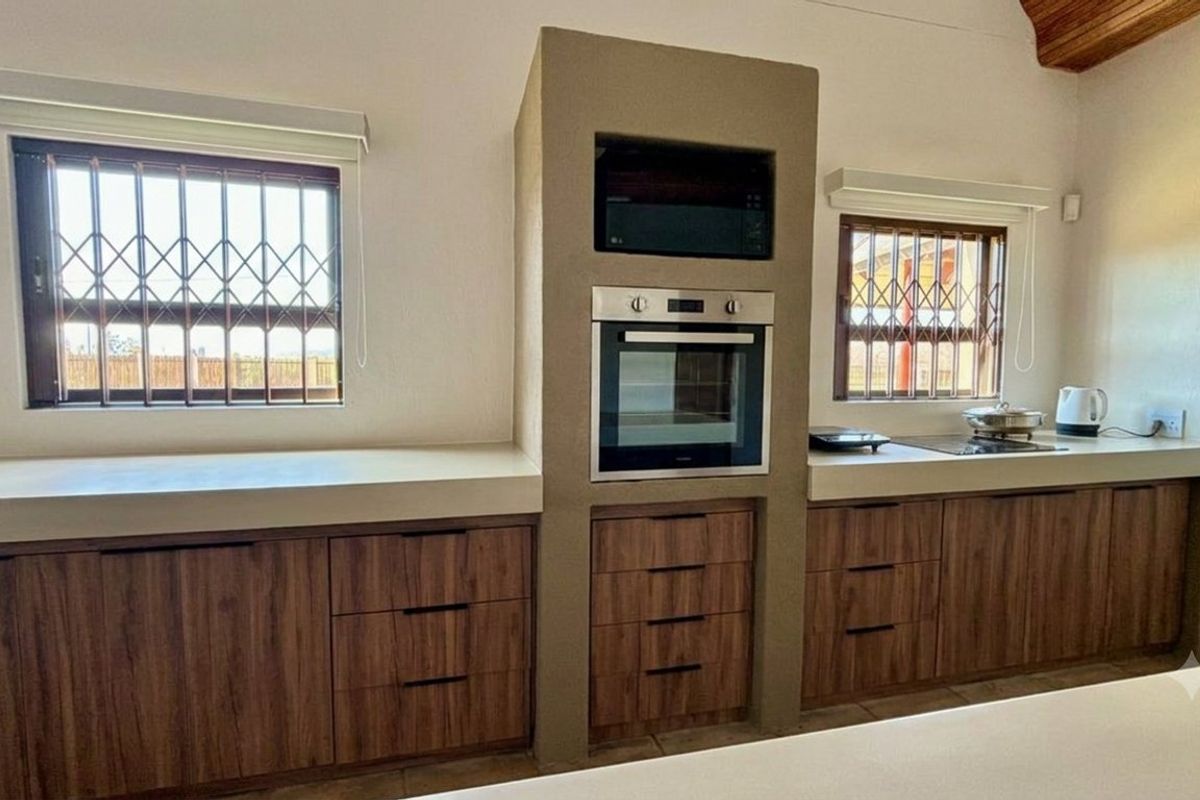 A well-maintained kitchen featuring wood-finish cabinetry, stone countertops, and integrated oven and microwave units, complemented by windows with security bars.