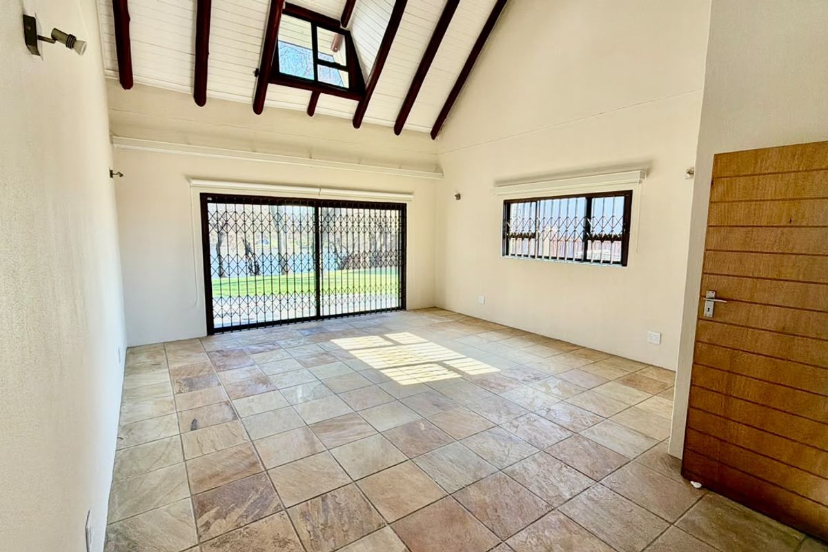 Spacious living area featuring vaulted ceilings with exposed timber beams, stone tile flooring, and large sliding doors leading to the garden.