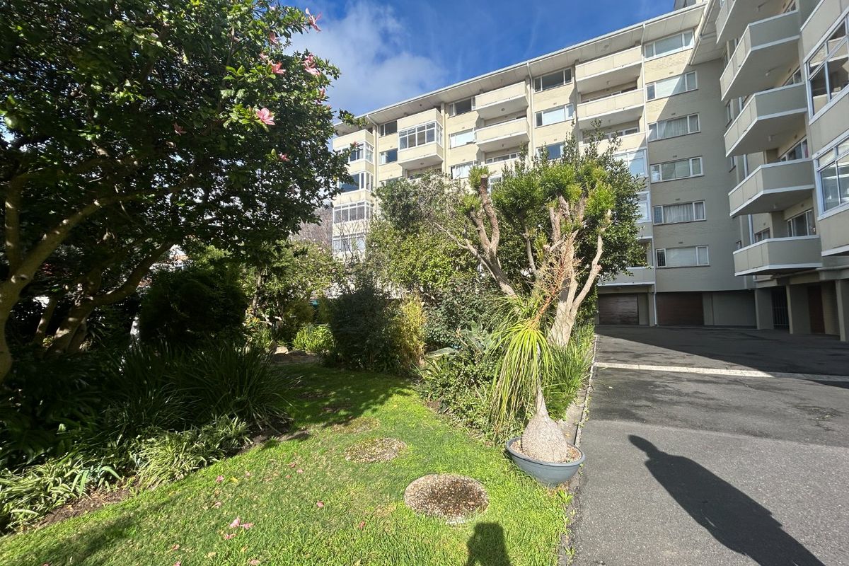 Exterior view of a multi-story apartment building featuring a landscaped garden area, paved driveway, and private balconies.