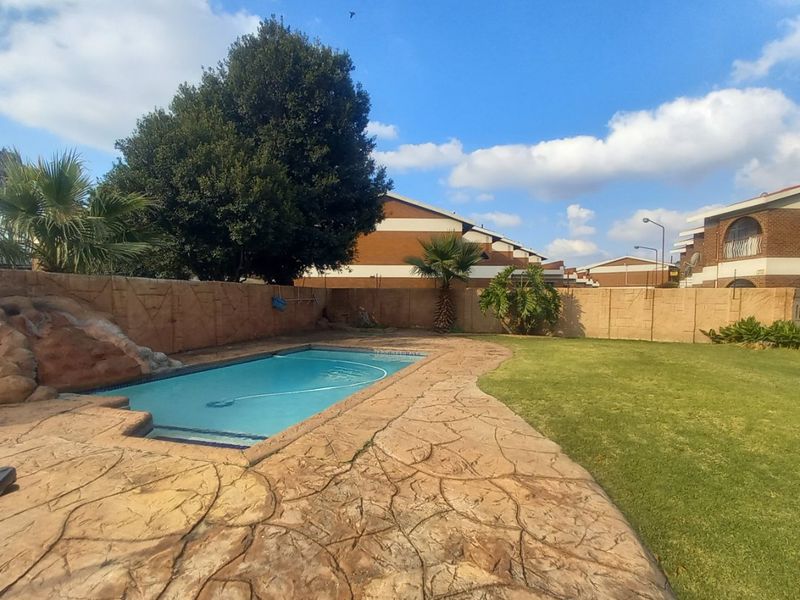 Outdoor pool area featuring a swimming pool with a rock feature, surrounded by a paved deck and a well-maintained lawn.