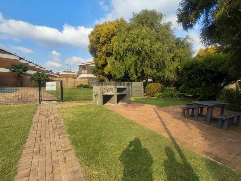 Communal outdoor area featuring a built-in braai, brick-paved patio, and landscaped garden space adjacent to the swimming pool enclosure.