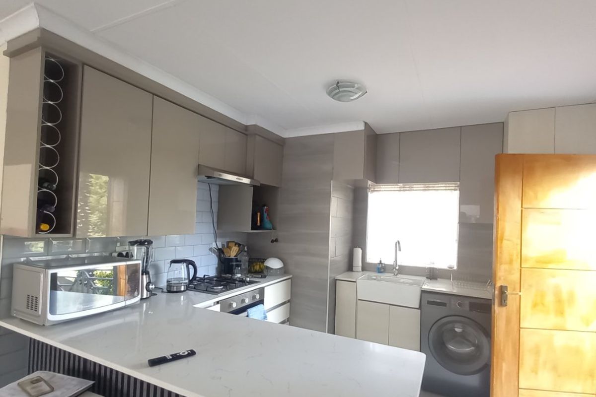 Modern kitchen featuring sleek cabinetry, quartz countertops, a gas hob, extractor fan, and a classic apron sink with integrated laundry space.