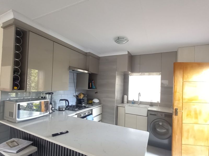 Modern kitchen featuring sleek cabinetry, quartz countertops, a gas hob, extractor fan, and a classic apron sink with integrated laundry space.