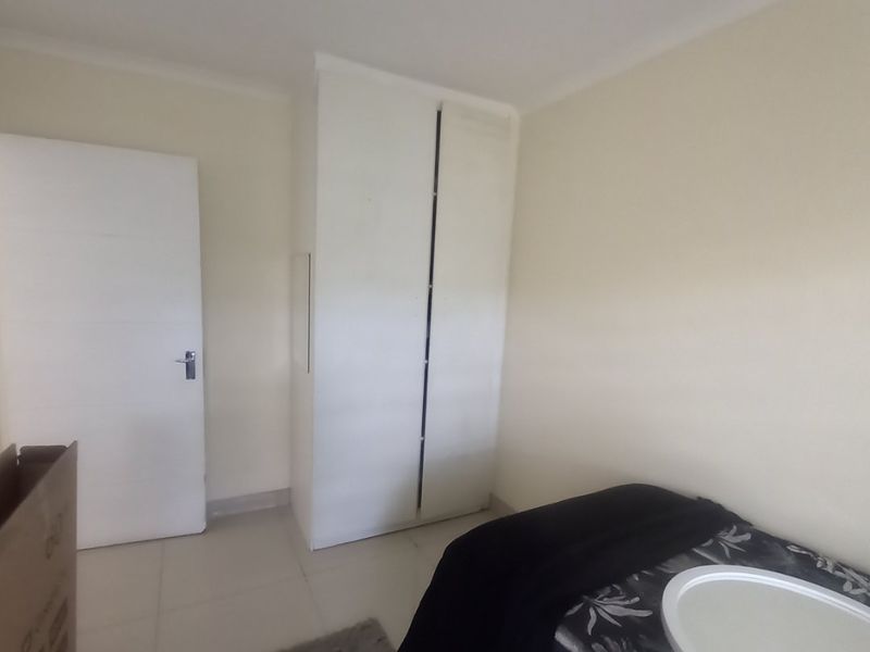 A clean bedroom featuring neutral walls, tiled flooring, and a built-in wardrobe, offering a simple and functional living space.