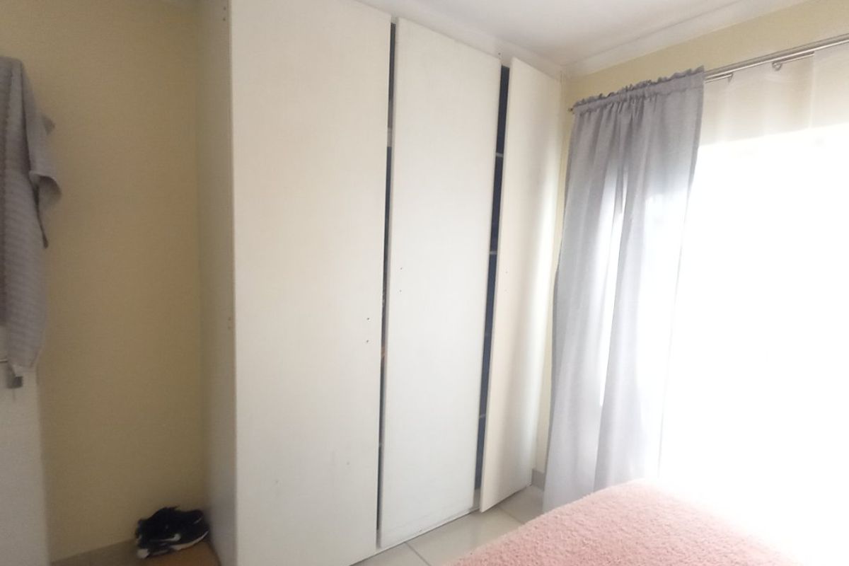 A bedroom featuring built-in wardrobes and tiled flooring, with natural light entering through the window.