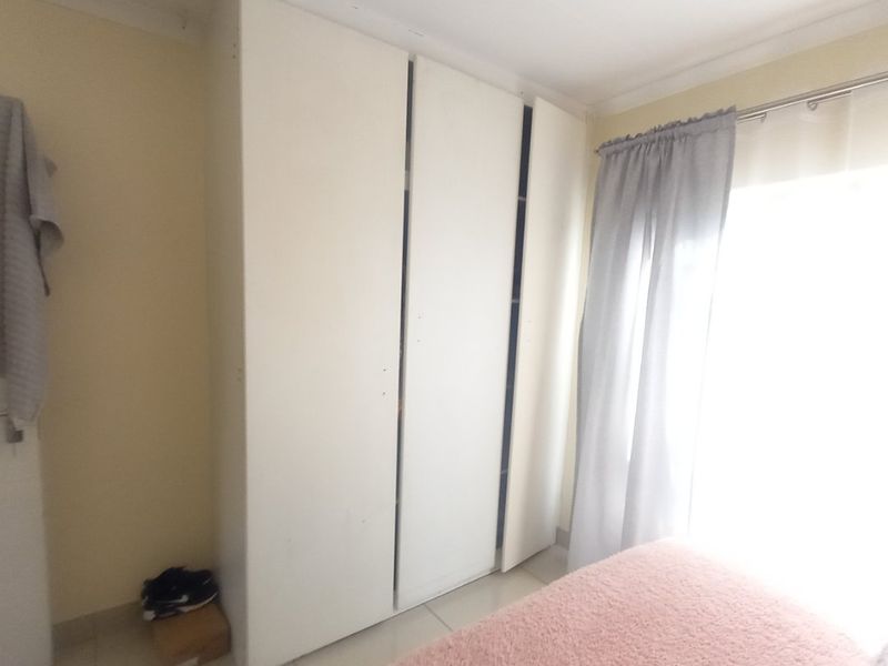 A bedroom featuring built-in wardrobes and tiled flooring, with natural light entering through the window.
