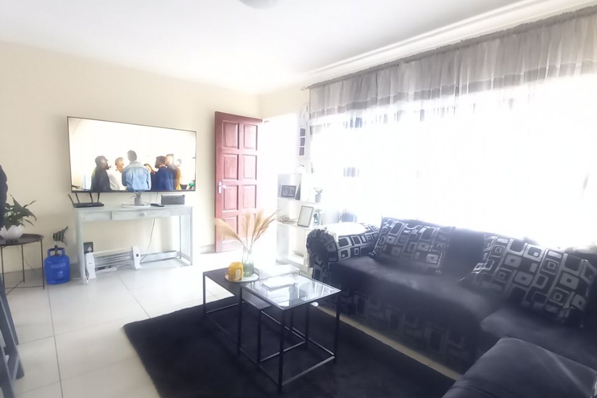 A bright living room featuring tiled flooring, a ceiling light fixture, and a panel door, with large windows allowing for ample natural light.