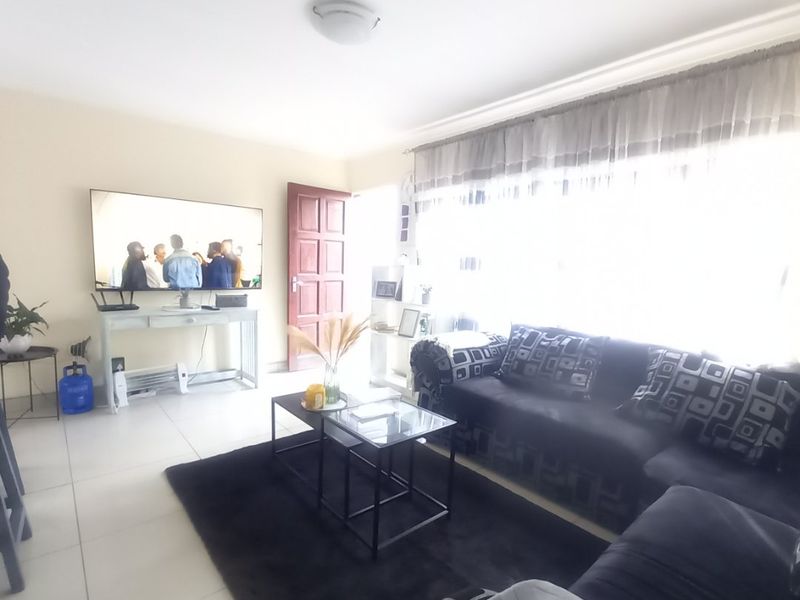 A bright living room featuring tiled flooring, a ceiling light fixture, and a panel door, with large windows allowing for ample natural light.