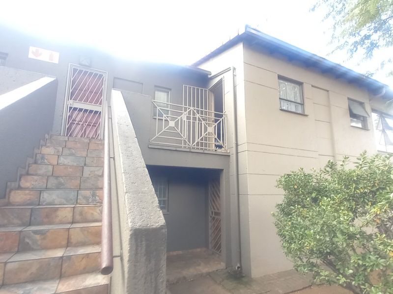 Exterior view of an apartment building featuring a tiled staircase, metal security gates, and a balcony with metal railings.