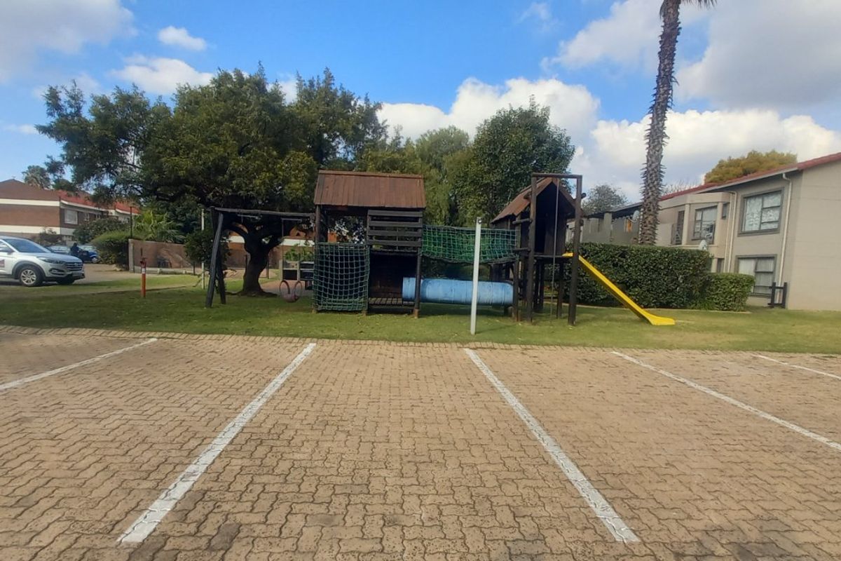 Communal outdoor area featuring a paved parking lot and a children's playground set within a landscaped garden space.