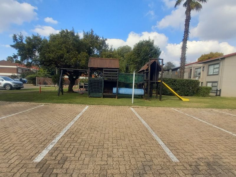 Communal outdoor area featuring a paved parking lot and a children's playground set within a landscaped garden space.