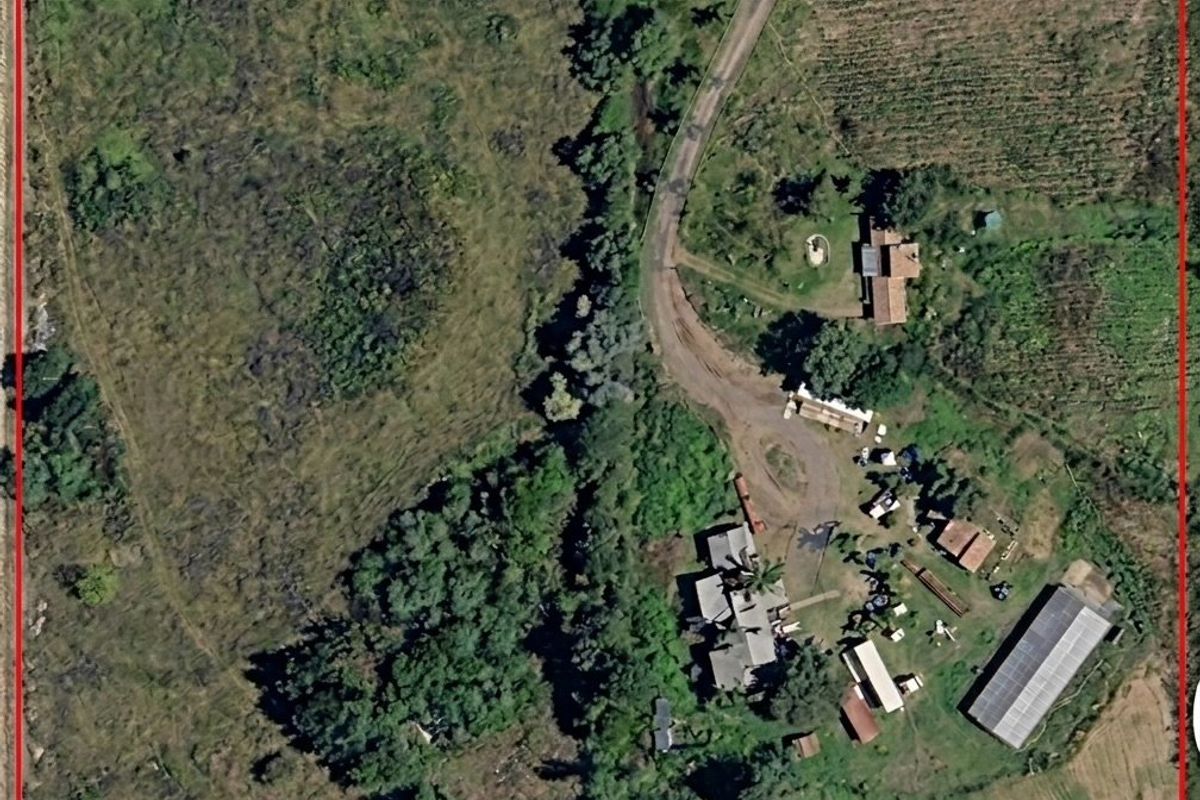 Aerial view of a large residential vacant land plot featuring natural vegetation, an access road, and existing outbuildings.
