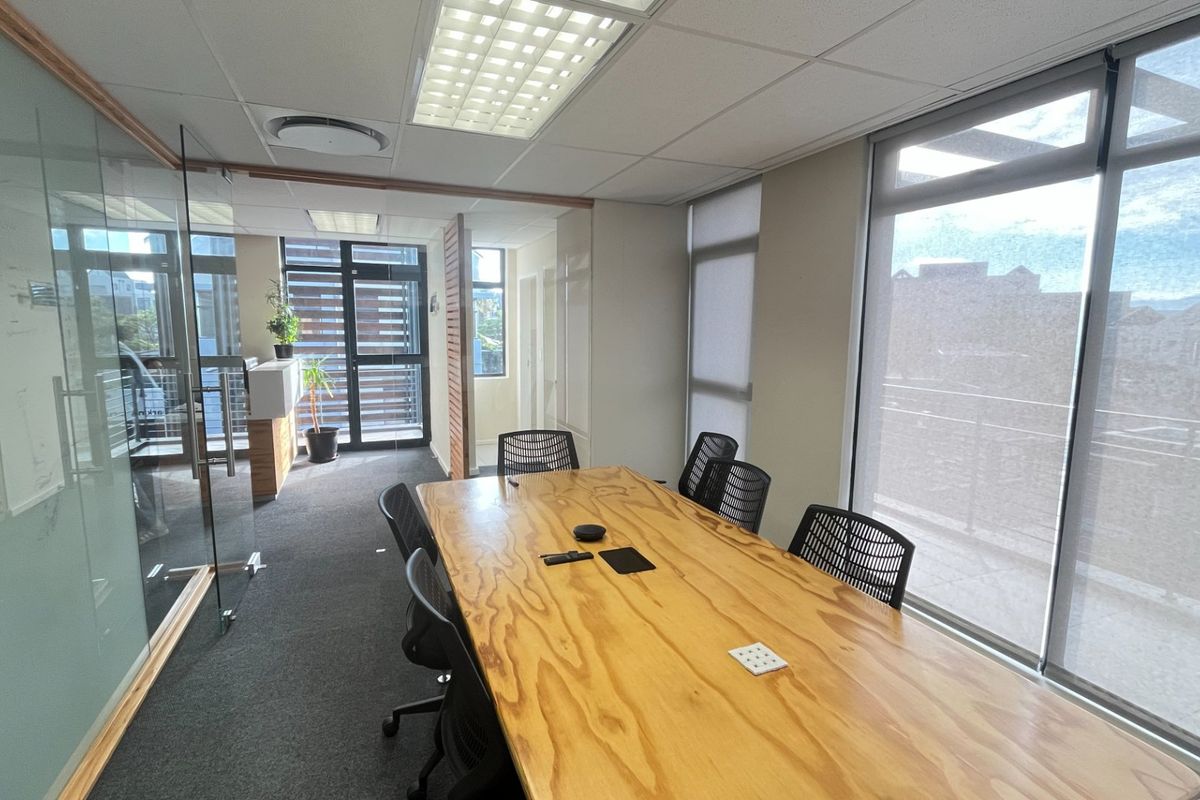 Modern commercial office space featuring glass partitions, large windows with roller blinds, carpeted flooring, and a professional suspended ceiling layout.