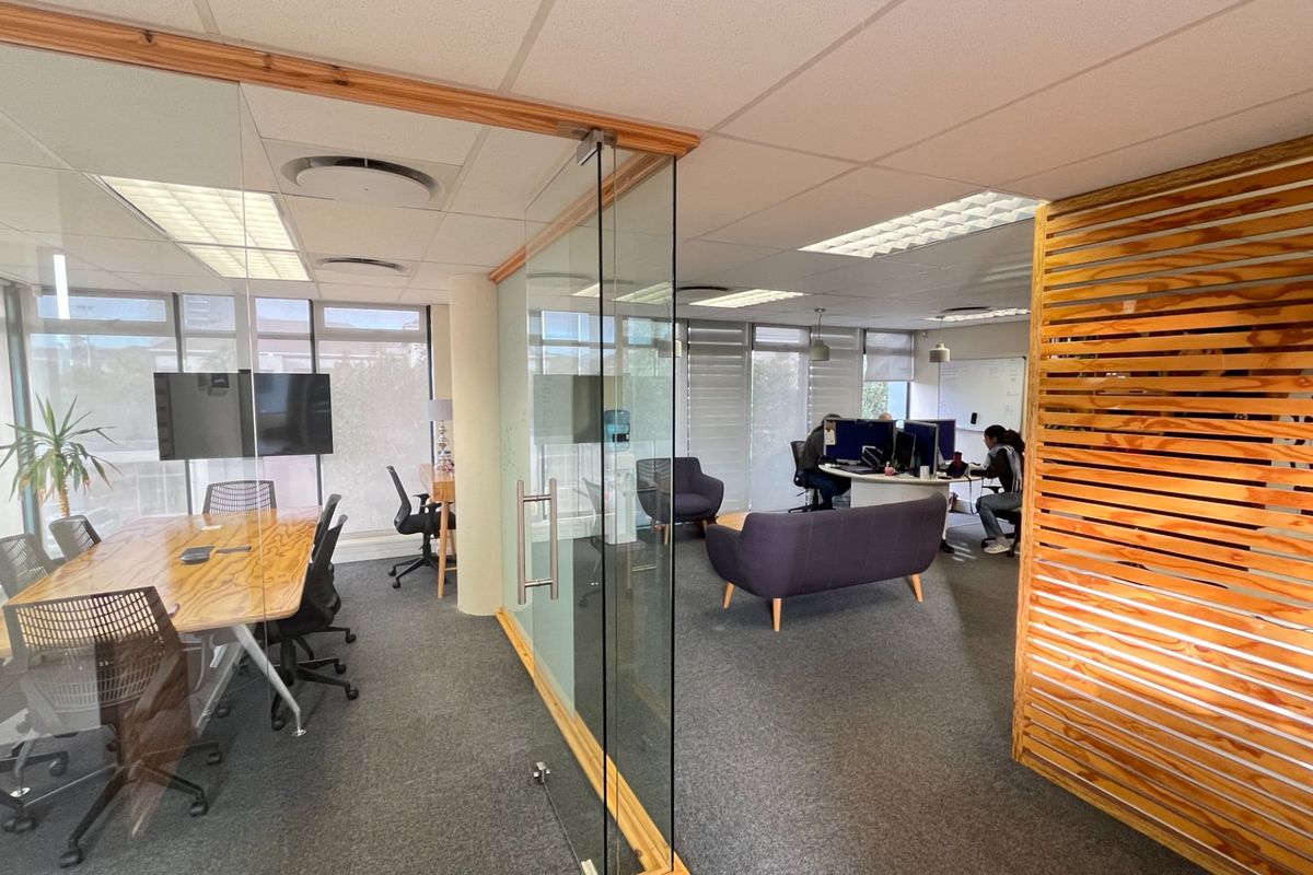 Modern commercial office space featuring glass partitions, timber slat accents, suspended ceilings, and large windows providing ample natural light.