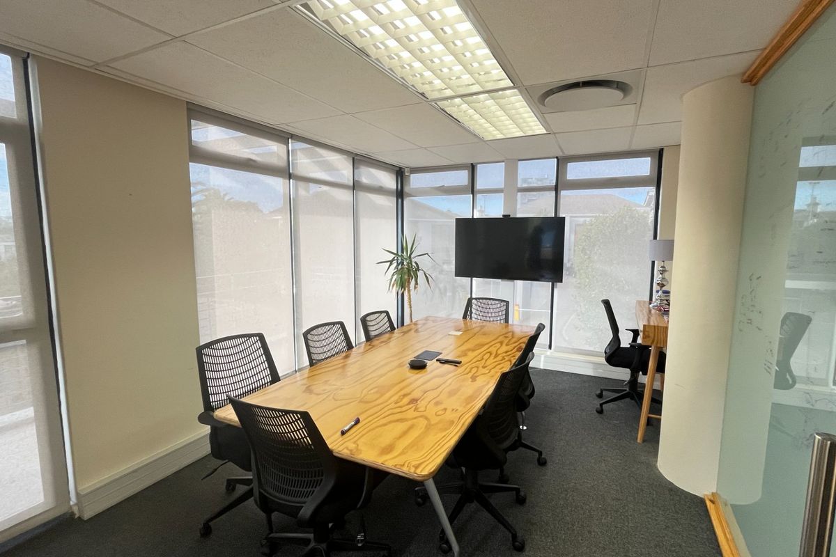 A professional office meeting room featuring large windows with roller blinds, a suspended ceiling with recessed lighting, and a glass partition wall.