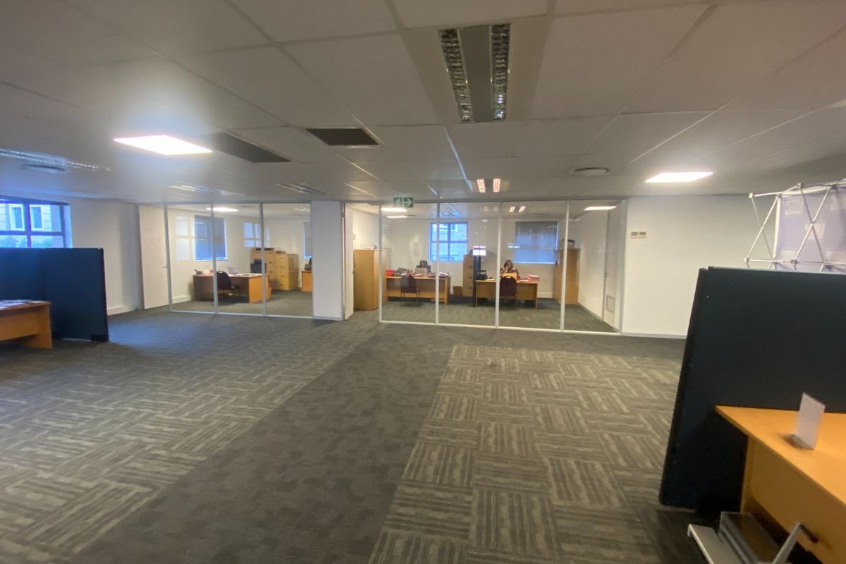Commercial office space featuring modular carpet tiles, suspended ceilings with recessed lighting, and glass-partitioned private offices.