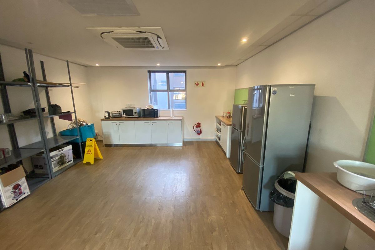 A functional commercial kitchen area featuring built-in cabinetry, laminate flooring, and integrated ceiling air conditioning, suitable for office or staff breakroom use.