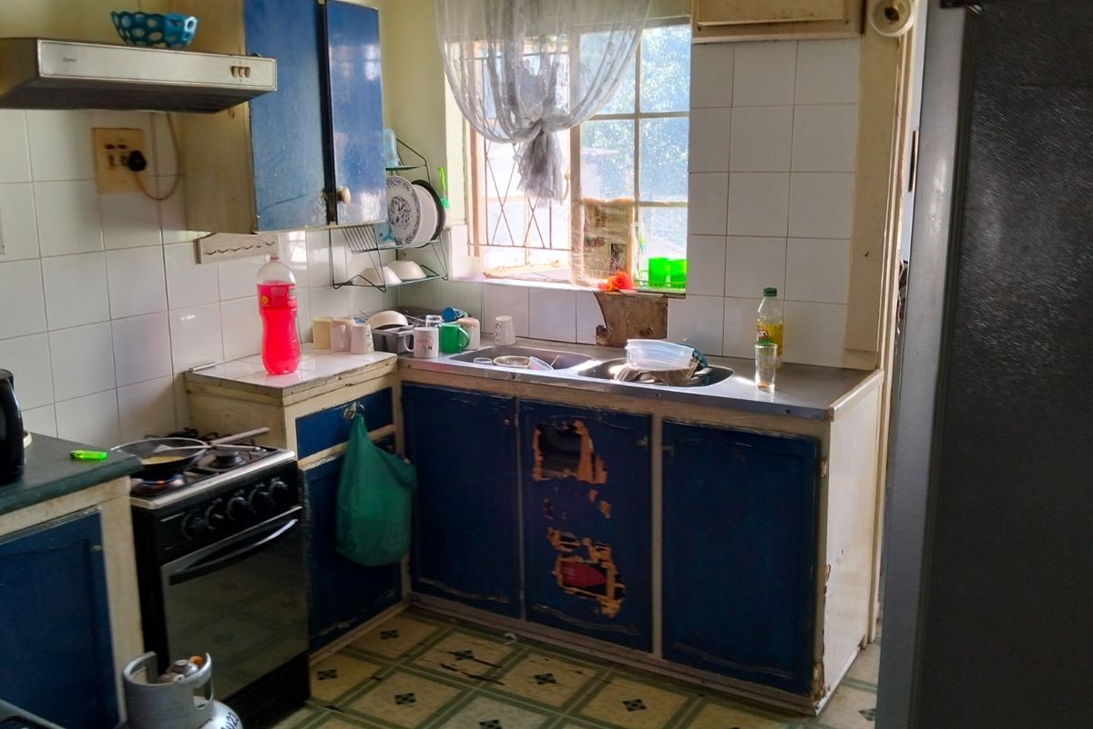 A dated kitchen featuring blue cabinetry, a stainless steel sink, and a gas stove, requiring significant cosmetic updates and repairs to the cabinetry.