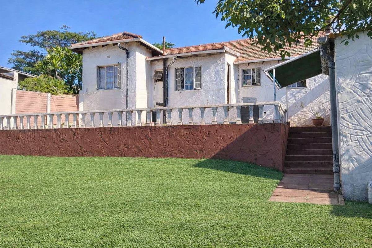 Rear view of the house featuring a raised patio with a concrete balustrade, textured exterior walls, and a large lawn area.