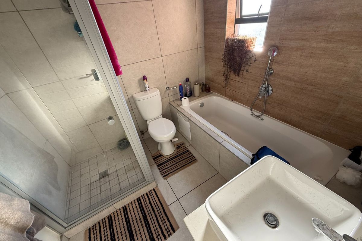A functional bathroom featuring a separate shower enclosure, a bathtub with handheld mixer, and a modern vessel sink with tiled finishes throughout.