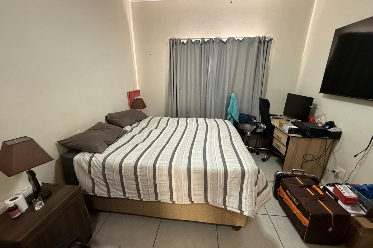 A functional bedroom featuring tiled flooring and a wall-mounted television, offering a practical layout for comfortable living.