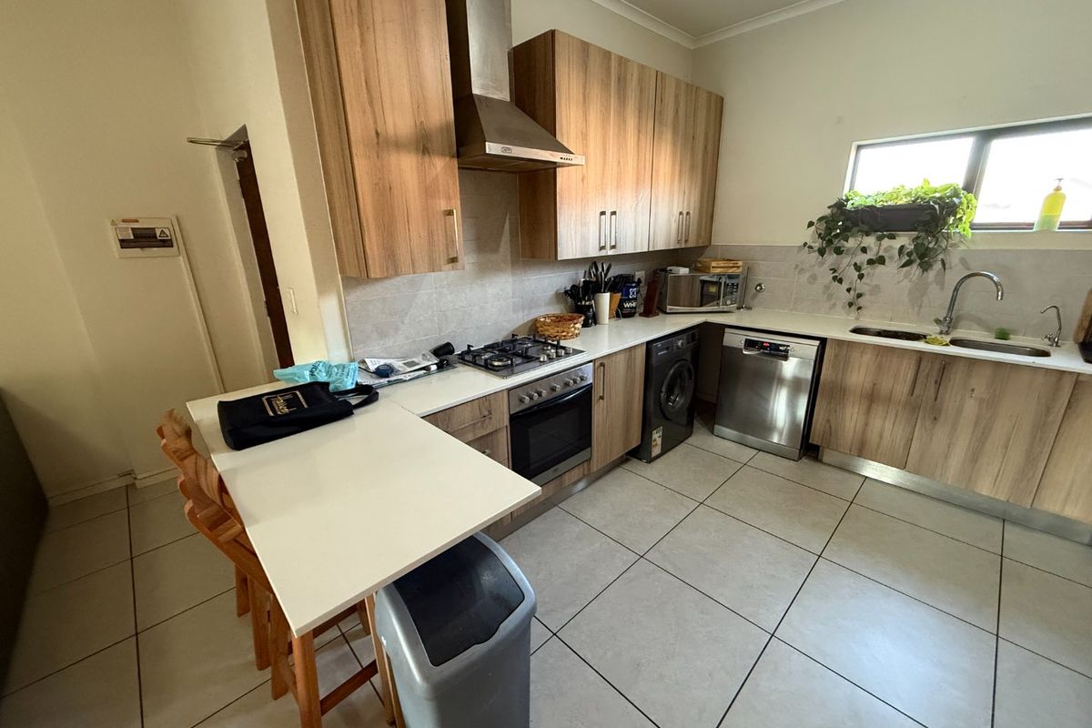 A functional kitchen featuring wood-finish cabinetry, a gas hob with extractor, integrated oven, and a breakfast counter with tiled flooring.