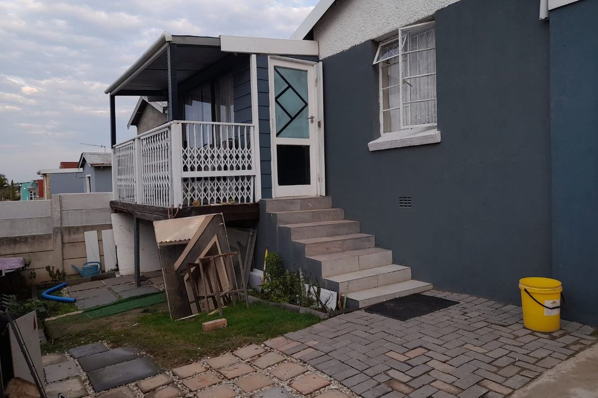 Rear exterior view showing a raised patio with security gate, paved ground area, and staircase leading to the main house structure.
