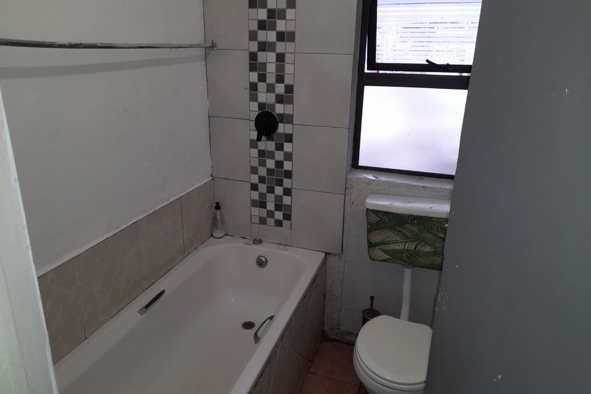 A compact bathroom featuring a bathtub, toilet, and tiled splashback. The space requires cosmetic updates to the wall finishes and tiling.