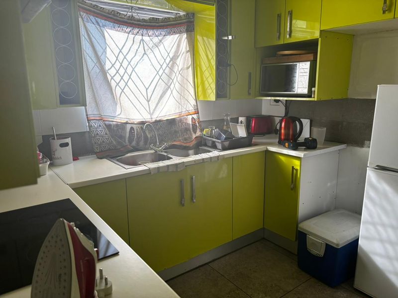 Compact kitchen featuring lime green cabinetry, stainless steel sink, electric hob, and built-in microwave with unfinished wall tiling.