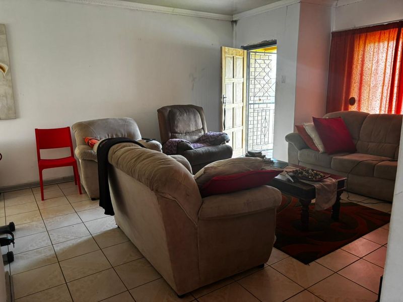 A living room featuring tiled flooring and a security gate entrance, showing signs of wear on the walls.