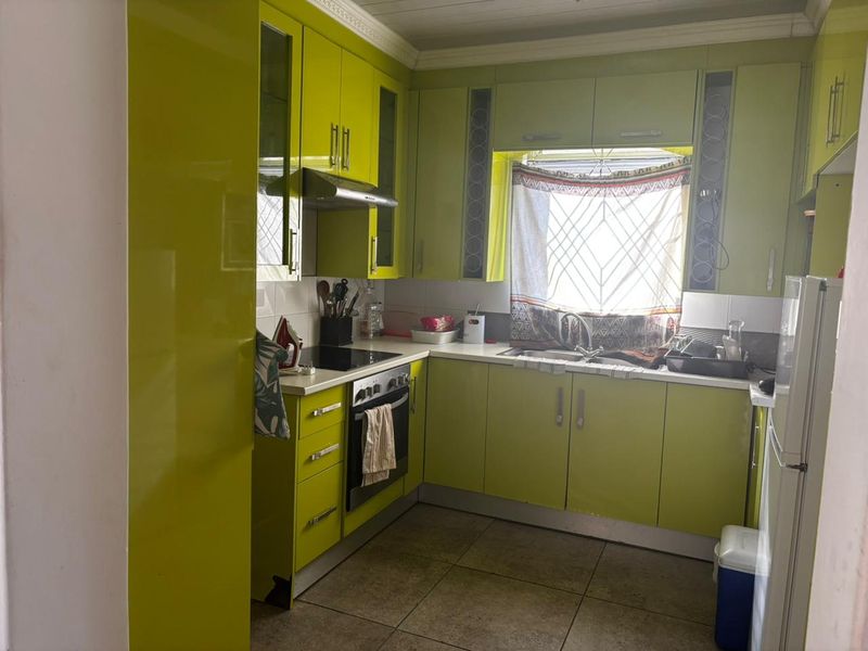 A functional kitchen featuring lime green cabinetry, built-in oven, extractor fan, and tiled flooring, offering a bright and practical workspace.