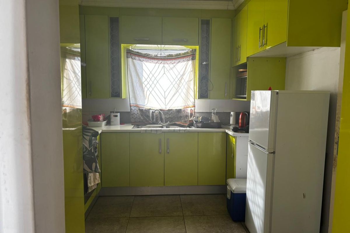 Compact kitchen featuring high-gloss lime green cabinetry, tiled flooring, and a central window above the sink area.