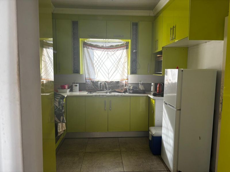 Compact kitchen featuring high-gloss lime green cabinetry, tiled flooring, and a central window above the sink area.