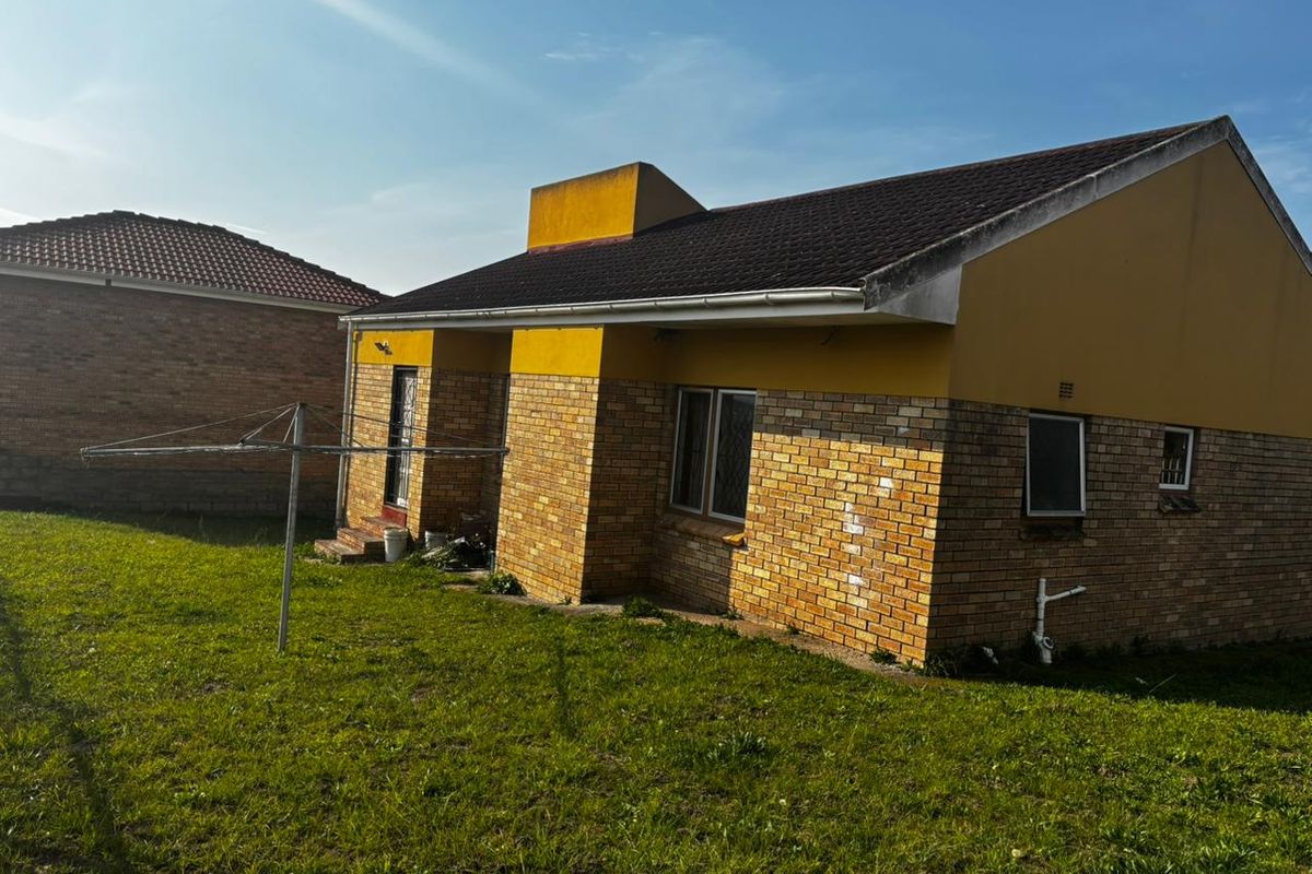 Rear view of a brick-faced house featuring a tiled roof, external plumbing, and a surrounding garden area.