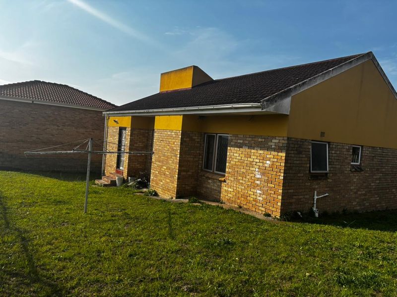 Rear view of a brick-faced house featuring a tiled roof, external plumbing, and a surrounding garden area.