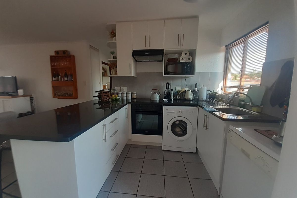 A functional kitchen featuring white cabinetry, black stone countertops, integrated oven and hob, and tiled flooring with a convenient breakfast bar area.