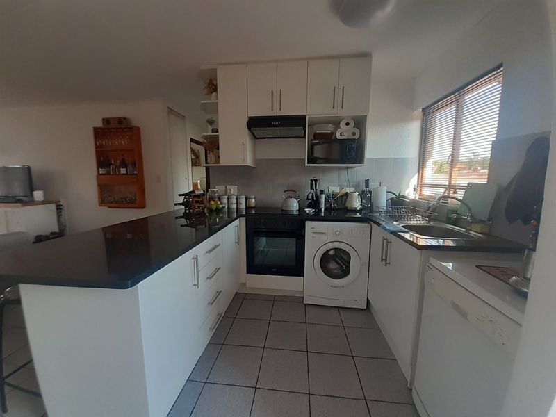 A functional kitchen featuring white cabinetry, black stone countertops, integrated oven and hob, and tiled flooring with a convenient breakfast bar area.
